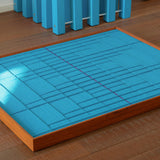 High-angle view of the blue geometric fiber art lying flat on a wooden floor, emphasizing the depth and structure of the woven pattern.