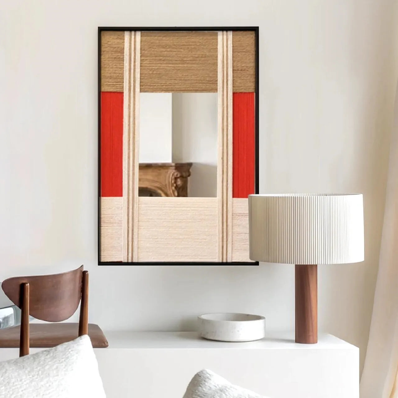 The Sun Always Rises hand-woven yarn mirror wall art with central reflective panel, oatmeal and natural wool stripe borders, and a bold red accent stripe, framed in black wood and displayed on a console table.