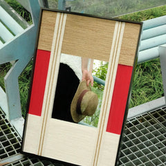 The Sun Always Rises yarn mirror art placed leaning on a metal grate, showcasing the seamless join between oatmeal and bold red wool stripe panels.