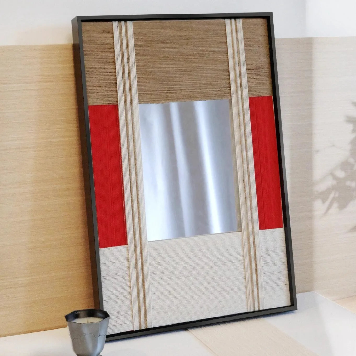 The Sun Always Rises mirror art resting on the floor beside a side table and cup, displaying its bold red stripe and clean wool panel layout in a modern interior.