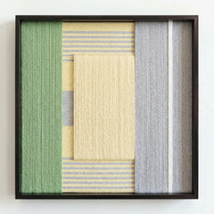 Frontal studio shot of a variant of the Sun-Baked hand-woven wool wall art featuring muted grey and green tones in a black frame.