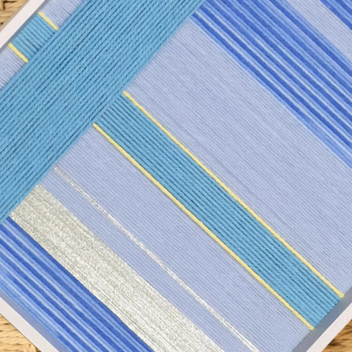 Flat lay of That Summer, the Blue Sea yarn wall art revealing its precise square form and uniform blue stripe weave