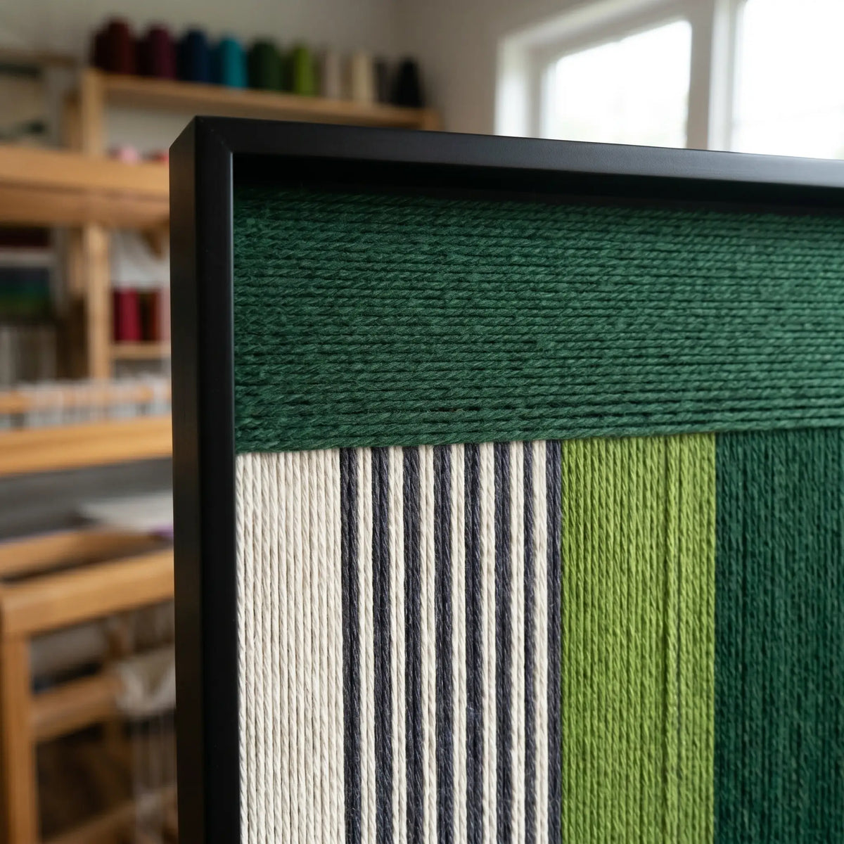 Side profile of the green and neutral soft cotton cord wall art in a workshop setting, showcasing the depth of the woven threads.