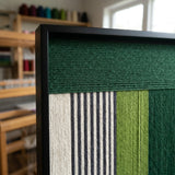 Side profile of the green and neutral soft cotton cord wall art in a workshop setting, showcasing the depth of the woven threads.
