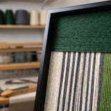Close-up shot of the top corner of the framed fiber art showing the horizontal and vertical soft cotton cord textile patterns.