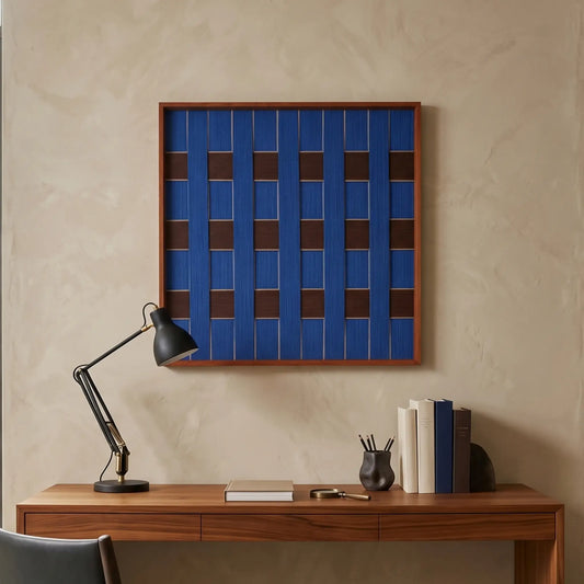 Square hand-woven wool wall art featuring a deep navy blue and brown woven grid pattern hanging above a wooden desk with a black architect lamp.