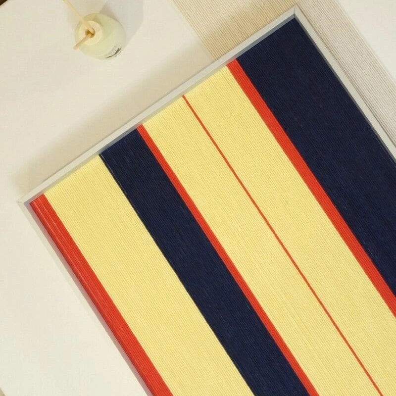 Close-up of Twilight Rush wool yarn wall art showing tight looped stitching and vivid coral accent against cream and navy stripe panels.