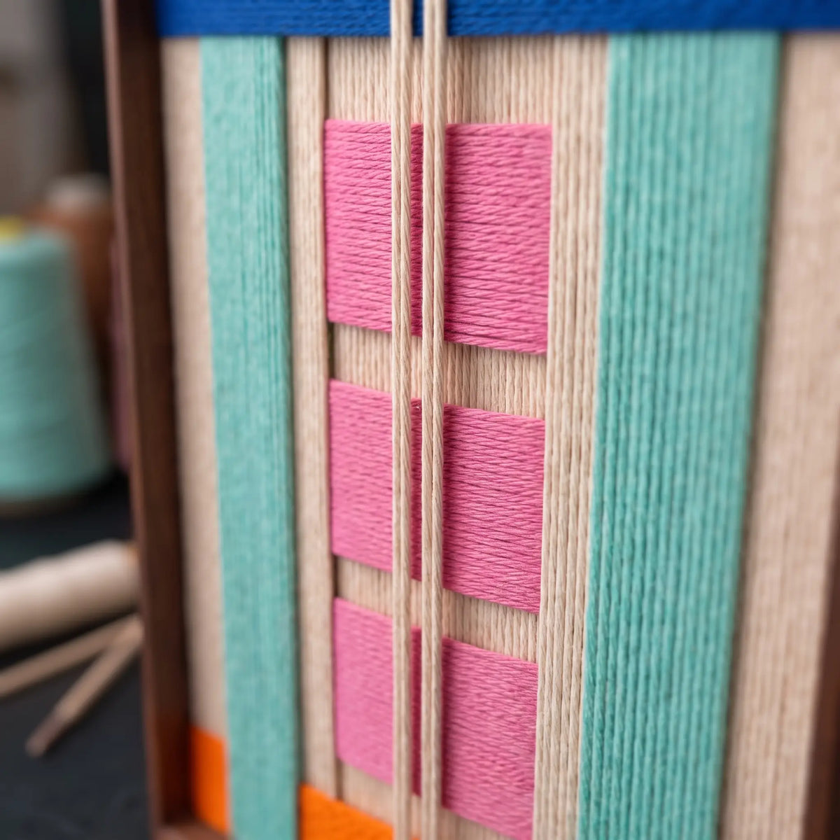 A detailed macro close-up of the Vegas Strip hand-woven wool tapestry featuring rich pink, teal, and orange geometric fibers.