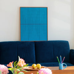 A focused shot of the framed blue wool tapestry resting on a plush sofa, highlighting the rich color saturation and modern design.