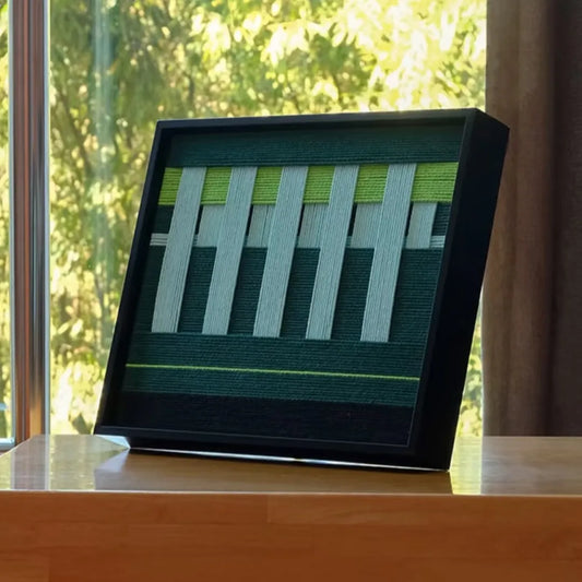 Velvet Vine hand-woven wool yarn wall art with alternating lime green and white vertical stripes in a sleek black frame, showcasing precise geometric design