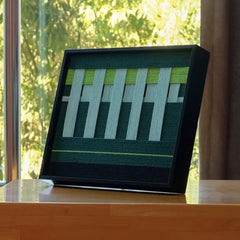 Velvet Vine hand-woven wool yarn wall art with alternating lime green and white vertical stripes in a sleek black frame, showcasing precise geometric design