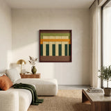 Framed fiber art tapestry with a forest green and earth tone design displayed in a sunlit interior with a cream sofa and neutral rug.