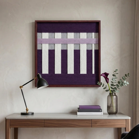 Hand-woven wool wall art with deep purple and white geometric textures hanging above a modern wooden desk with a black lamp.