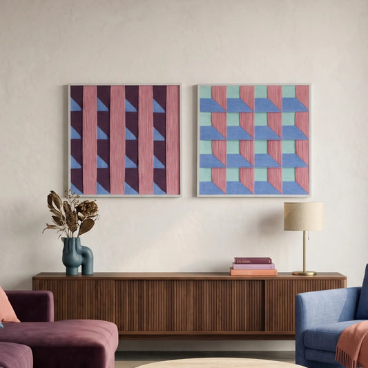 A pair of square hand-woven wool wall art pieces featuring 3D-effect geometric brick patterns in pink, purple, and teal, hanging above a mid-century modern walnut sideboard.