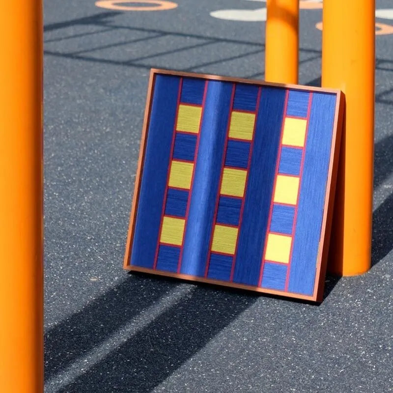 Window Peek at Moon yarn woven art placed on a street bollard in daylight, featuring crisp stair-step gradient from azure to sky blue