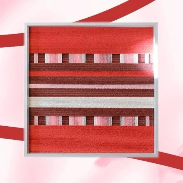 Framed geometric fiber wall art in red, burgundy, pink, and white on a pink background.