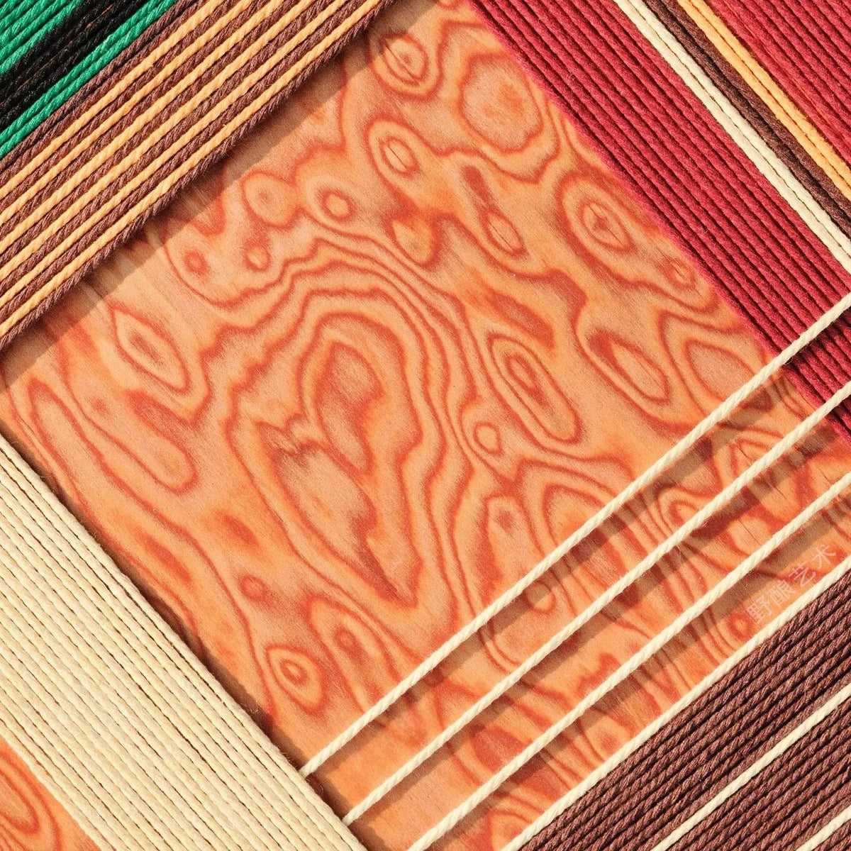 Close-up of Christmas Melody fiber wall art showing red, green, cream and brown cord lines surrounding a warm wood-grain pattern