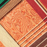 Close-up of Christmas Melody fiber wall art showing red, green, cream and brown cord lines surrounding a warm wood-grain pattern