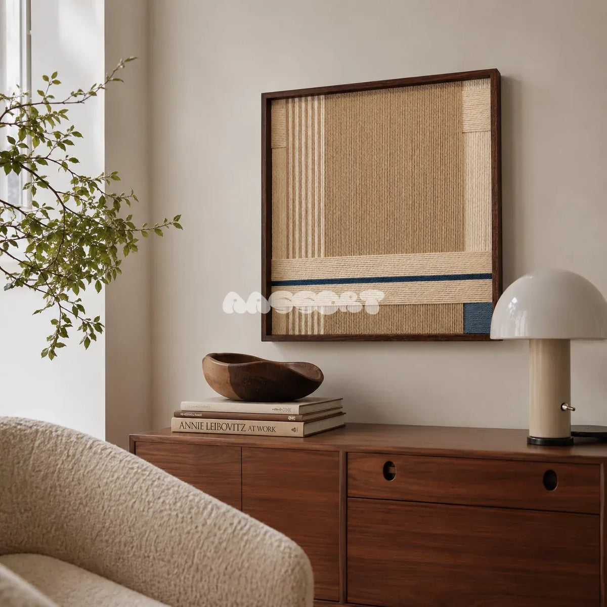 A Collected Morning cream, toasted sand, and indigo yarn wall art displayed above a wood cabinet beside a curved cream chair in a reading corner.