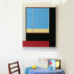 After the Beach Walk hand-woven wool yarn wall art with coastal-blue top panel, golden-sand middle stripe, sunset-red bottom block, and bold black side panel in a natural wood frame
