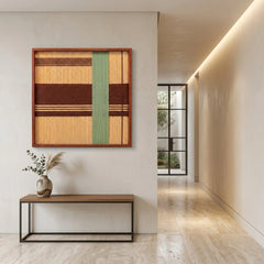 Large square Amber Pine textile wall art featuring woven tan, dark brown, and sage green geometric patterns, hanging above a minimalist console table in a modern hallway.
