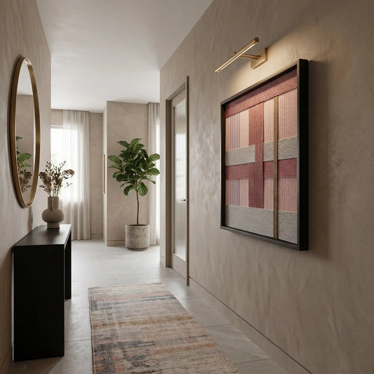 Large square hand-woven wool wall art in shades of pink, mauve, and grey hanging in a modern hallway with a gallery light and minimalist console.
