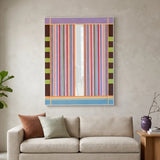 Large vertical hand-woven wool wall art featuring a vibrant striped pattern in pink, purple, and blue with a central mirror inlay, hanging above a contemporary beige sofa.