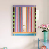 Blooming Flowers hand-woven wool yarn wall art featuring alternating pastel pink, coral, mint, and sky-blue vertical stripes in a natural wood frame, displayed above a console table with vase and books.
