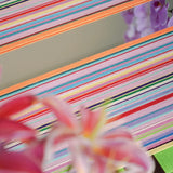 Hand-held view of Blooming Flowers yarn wall art in front of greenery, emphasizing its compact square form, rich looped texture, and multicolor stripe interplay.
