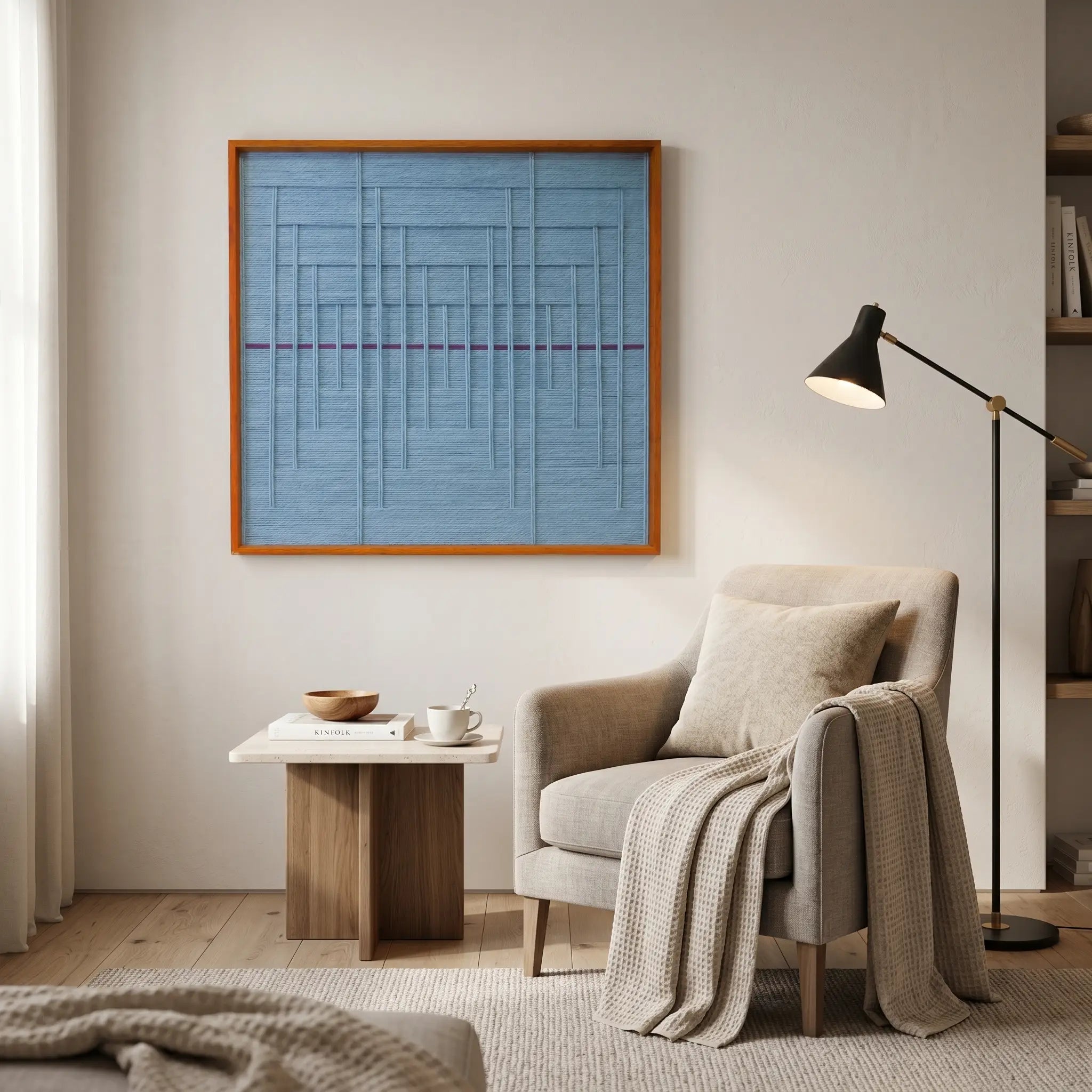Framed light blue textile art displayed in a cozy reading corner above a light beige armchair and a modern black floor lamp.