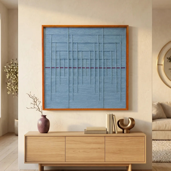 Large square Blue Bridge Over the Pond textile wall art featuring a light blue woven background with a red horizontal stripe, hanging above a light oak sideboard in a sunlit living room.