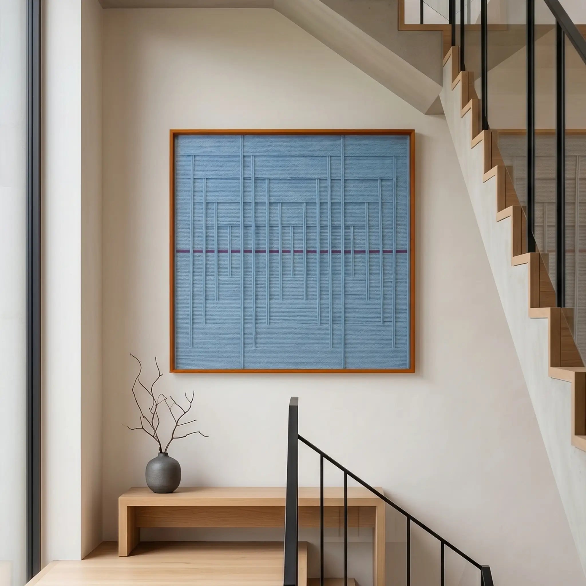 Square light blue woven textile art creating a serene focal point on a bright white staircase landing above a low wooden bench.