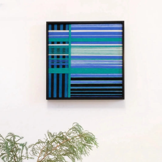 Blues Harmony hand-woven wool yarn wall art in alternating navy, sky blue, and dove grey vertical stripes, framed in sleek black wood, displayed on a console tabletop
