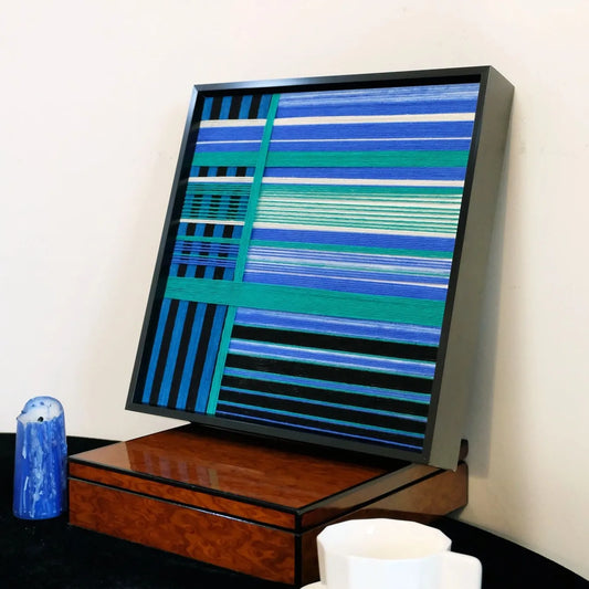 Blues Harmony yarn woven art styled on a desk next to a soda can and glass, highlighting its precise stripe alignment and modern frame

