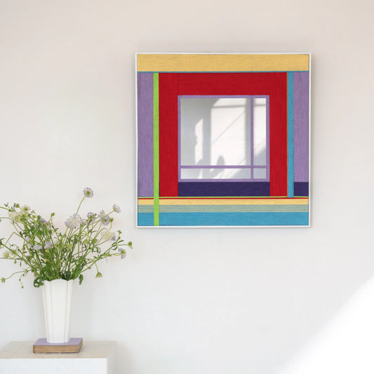 Bohemian Reverie yarn mirror art styled above a potted plant, showcasing its vibrant pastel and red stripe composition.
