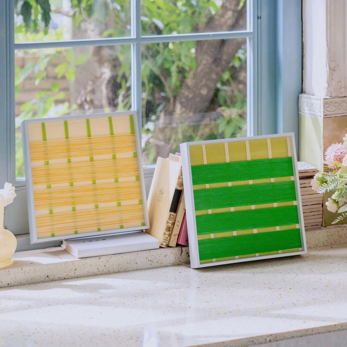 Styled view of the hand-woven art pieces leaning against a window with books, creating a cozy and artistic atmosphere suitable for reading nooks.
