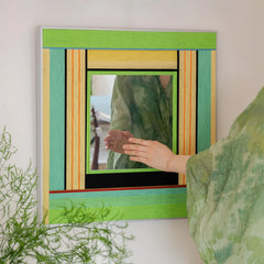 Hand‑held view of Breathing Like Fresh Grass yarn mirror art being hung, highlighting its lightweight frame and easy installation.
