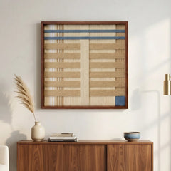 Large square hand-woven wool wall art with neutral and blue horizontal patterns hanging above a dark walnut sideboard in a warm minimalist living room.