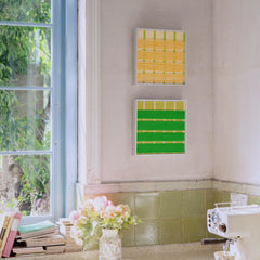 A wider view of the Spring Breeze wool tapestry set hanging on a white wall, adding a pop of vibrant color to a bright, sunlit room.