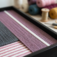 Detailed macro shot of Burgundy Overture hand-woven wool art showing the deep plum, charcoal grey, and striped pink yarn textures in a black frame.