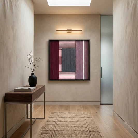 Square burgundy and charcoal textured fiber art hanging in a minimalist hallway above a wood console table with a gallery light.