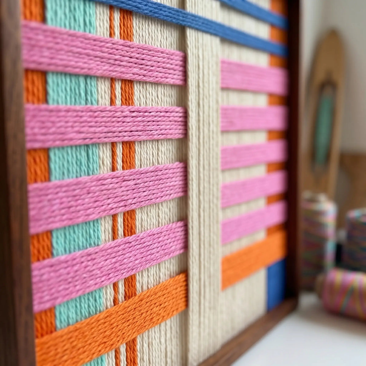 Close-up macro shot of the California Afterglow fiber art highlighting the bright pink, orange, and blue soft cotton cord and structural layering within a wooden frame.