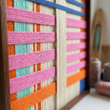Close-up macro shot of the California Afterglow fiber art highlighting the bright pink, orange, and blue soft cotton cord and structural layering within a wooden frame.