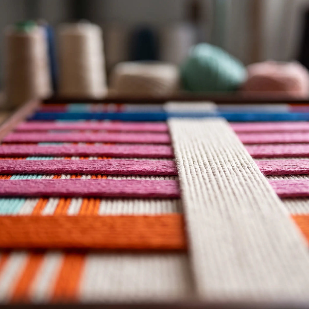Macro close-up view of the California Rhythm hand-woven wool tapestry highlighting the colorful pink, orange, and cream yarn texture.