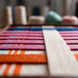 Macro close-up view of the California Rhythm hand-woven wool tapestry highlighting the colorful pink, orange, and cream yarn texture.