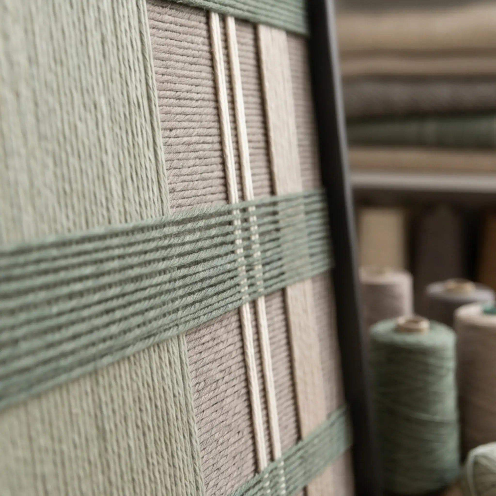 Angled close-up of the framed Celadon Mist hand-woven tapestry showcasing the black frame and dimensional green and beige geometric wool patterns.