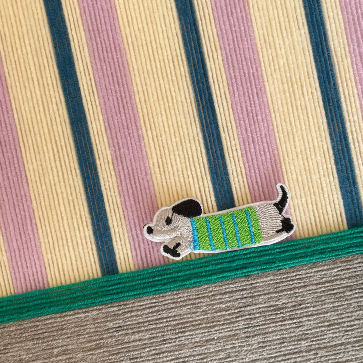 Macro shot of the soft cotton cord texture showing the raised cerulean and lavender stripes and the embroidered dog character detail.