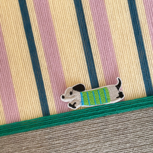 Macro shot of the hand-woven wool texture showing the raised cerulean and lavender stripes and the embroidered dog character detail.