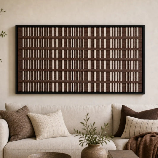 Large framed Cocoa Cadence hand-woven wall art hanging elegantly above a cozy beige sofa adorned with brown pillows in a warm living room.