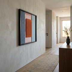 Vertical view of the red and blue textured fiber art hanging as a focal point in a minimalist modern hallway.